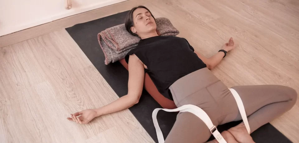 Mujer practicando yoga restaurativo en un estudio, usando almohadas y cintas para soporte, con una expresión de relajación en su rostro.